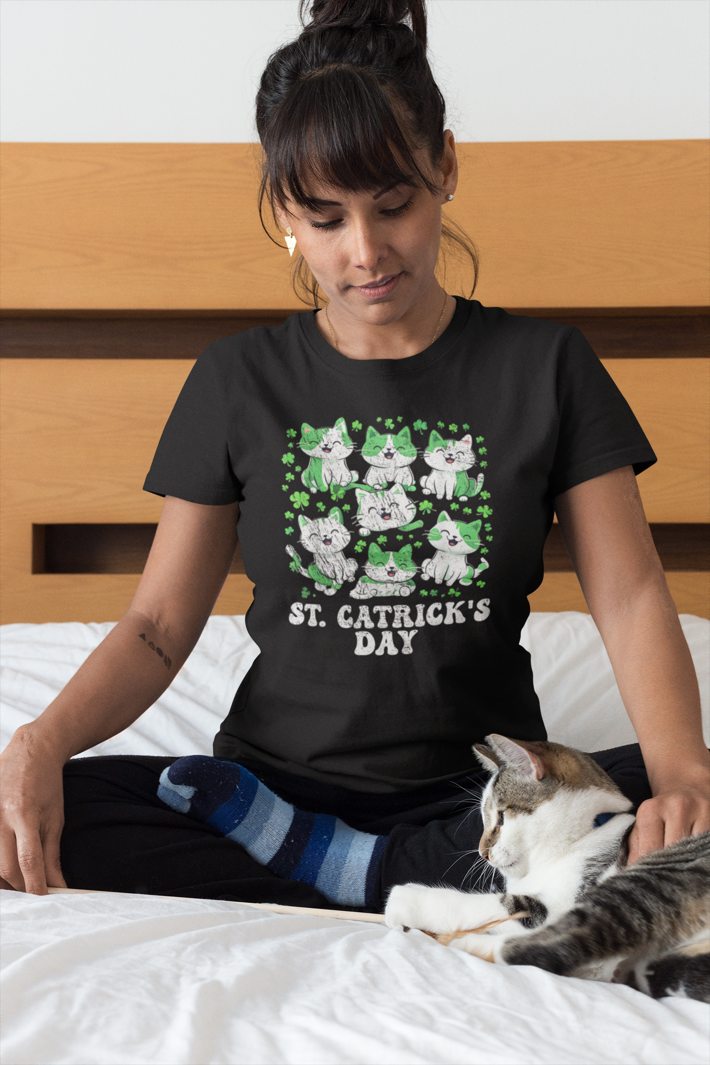 Woman wearing a black t-shirt with a cat-themed design, sitting on a bed with a cat.